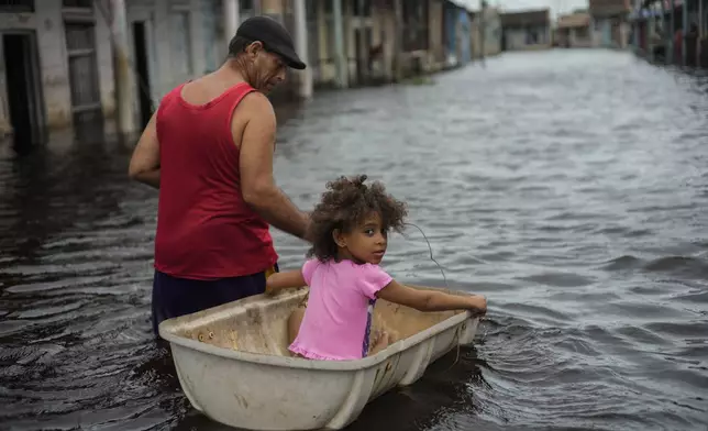 Jesus Hernandez guides his granddaughter Angelina via a container through a street flooded in the passing of Hurricane Helene, in Batabano, Mayabeque province, Cuba, Thursday, Sept. 26, 2024. (AP Photo/Ramon Espinosa)