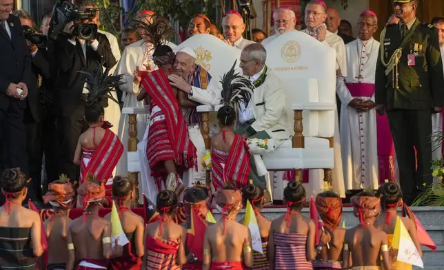 Pope Francis hugs a child in traditional dress as he attends with East Timor's President José Manuel Ramos-Horta, seated at right, a welcome ceremony outside the Presidential Palace in Dili, East Timor, Monday, Sept. 9, 2024. Pope Francis arrived in East Timor on Monday to encourage its recovery from a bloody and traumatic past and celebrate its development after two decades of independence from Indonesian rule. (AP Photo/Gregorio Borgia)