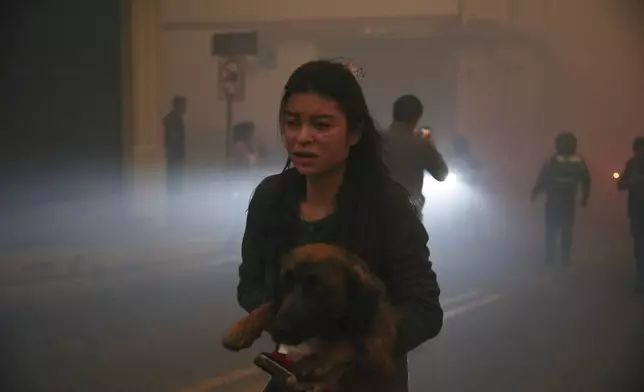 A resident carries a dog amid smoke from fires in a forested area in the Guapulo neighborhood of Quito, Ecuador, Tuesday, Sept. 24, 2024. (AP Photo/Carlos Noriega)