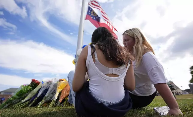 Two students view a memorial as the flags fly half-staff after a shooting Wednesday at Apalachee High School, Thursday, Sept. 5, 2024, in Winder, Ga. (AP Photo/Mike Stewart)