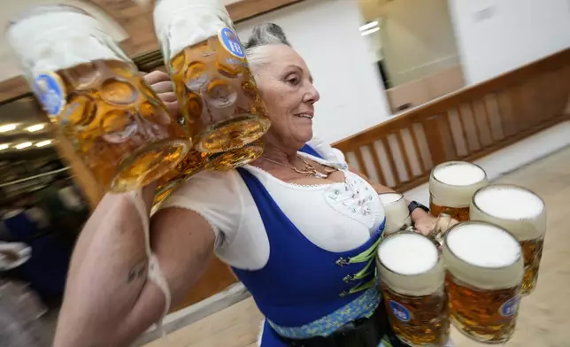 A waitress carrying beer mugs in the Hofbraeuhaus beer tent on day one of the 189th 'Oktoberfest' beer festival in Munich, Germany, Saturday, Sept. 21, 2024. (AP Photo/Matthias Schrader)