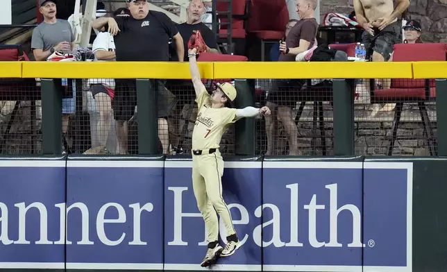 Arizona Diamondbacks right fielder Corbin Carroll reaches over the fence to make a catch on a fly ball hit by San Francisco Giants' Mike Yastrzemski during the second inning of a baseball game Tuesday, Sept. 24, 2024, in Phoenix. (AP Photo/Ross D. Franklin)