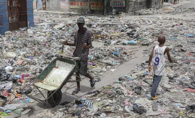 People walk down a street covered with trash in downtown Port-au-Prince, Haiti, Thursday, Sept. 5, 2024. (AP Photo/Odelyn Joseph)