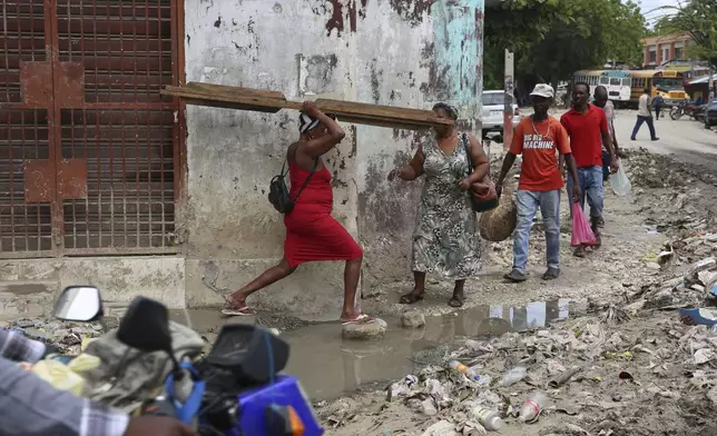 Pedestrians cross a puddle of water in downtown Port-au-Prince, Haiti, Monday, Sept. 23, 2024. (AP Photo/Odelyn Joseph)