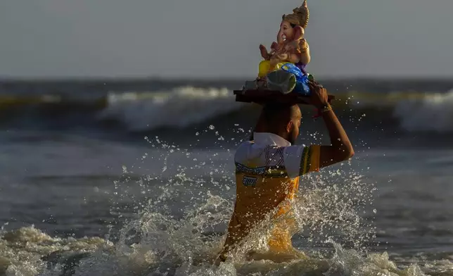 A devotee takes an idol of elephant-headed Hindu god Ganesha to immerse in the Arabian Sea, during the ten days long Ganesh Chaturthi festival in Mumbai, India, Sunday, Sept. 8, 2024. (AP Photo/Rafiq Maqbool)