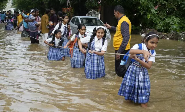 Students hold on to a rope as they cross a street flooded after heavy rains, on their way home in Ajmer, India, Friday, Sept. 6, 2024. (AP Photo/Deepak Sharma)