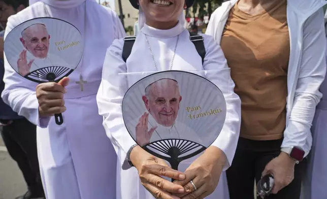 Devotees carrying hand fans printed with portraits of Pope Francis wait outside the Indonesian Bishops' Conference Headquarters to welcome the pope before his arrival for a meeting, in Jakarta, Indonesia, Thursday, Sept. 5, 2024. (AP Photo/ Tatan Syuflana)