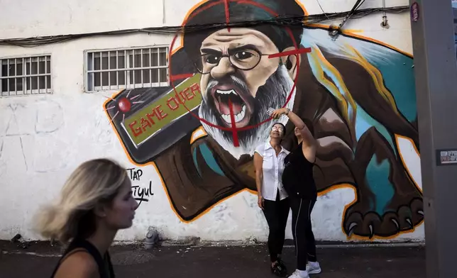 Two women take a selfie next to a newly painted graffiti of Hezbollah leader Hassan Nasrallah, a day after Hezbollah confirms its leader was killed in an Israeli airstrike, in Tel Aviv, Israel, on Sunday, Sept. 29, 2024. (AP Photo/Oded Balilty)