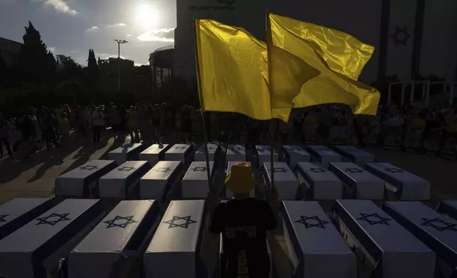 A man holds flags next to mock coffins covered in Israeli flags representing the 27 hostages whose bodies have been recovered from Gaza, during a rally demanding a cease-fire deal and the immediate release of hostages held by Hamas in the Gaza Strip on Thursday, Sept. 5, 2024, in Tel Aviv, Israel. (AP Photo/Ohad Zwigenberg)