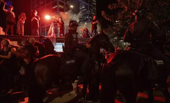 Demonstrators light flares as police on horses block their way during a protest demanding a cease-fire deal and the immediate release of hostages held by Hamas in the Gaza Strip on Thursday, Sept. 5, 2024, in Tel Aviv, Israel. (AP Photo/Ohad Zwigenberg)