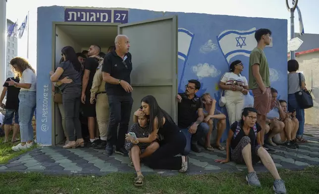 Israelis take cover next to a shelter as a siren sounds a warning of incoming rockets fired from Lebanon, in Nahariya, northern Israel, Thursday, Sept. 19, 2024. (AP Photo/Baz Ratner)