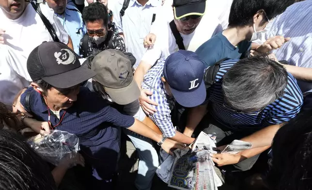 Pedestrians try to obtain an extra edition of the Sports Hochi newspaper reporting on the Los Angeles Dodgers' Shohei Ohtani becoming the first player in major league history with 50 home runs and 50 stolen bases in a season, Friday, Sept. 20, 2024, in Tokyo. (AP Photo/Eugene Hoshiko)