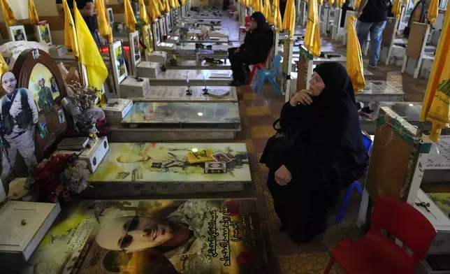 Women sit in a cemetery as they visit the graves of killed Hezbollah members in the southern suburbs of Beirut, Thursday, Sept. 19, 2024. (AP Photo/Hussein Malla)