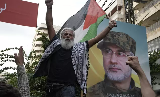 A Hezbollah supporter carries a Palestinian flag near a picture of Hezbollah commander Ibrahim Akil, during Akil's funeral procession in Beirut's southern suburb, Sunday, Sept. 22, 2024. (AP Photo/Bilal Hussein)