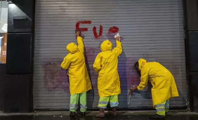 Workers remove a spray painted message accusing the government for the disappearance of 43 Ayotzinapa rural teacher's college students, after a demonstration marking the 10-year anniversary of their disappearance, in Mexico City, Thursday, Sept. 26, 2024. (AP Photo/Jon Orbach)