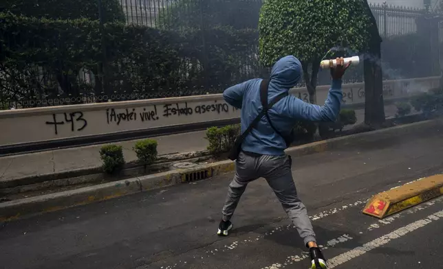 A hooded student throws an explosive at the Ministry of the Interior during demonstrations ahead of the 10th anniversary of the disappearance of 43 Ayotzinapa in Guerrero state, in Mexico City, Monday, Sept. 23, 2024. (AP Photo/Felix Marquez)