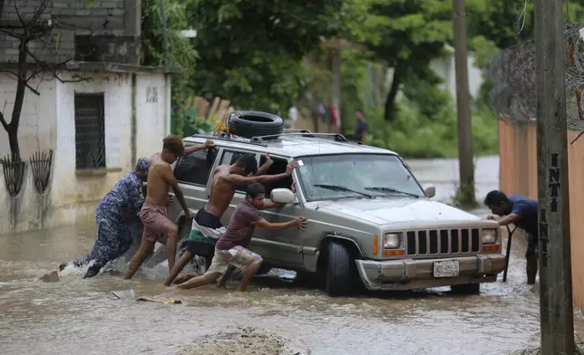 Residents work together to push a vehicle stuck on a street flooded by the passing of Hurricane John, in Acapulco, Mexico, Friday, Sept. 27, 2024. (AP Photo/Bernardino Hernandez)