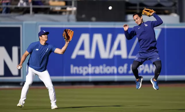 Los Angeles Dodgers interpreter Will Ireton, right, is unable to reach a batted ball while trying to protect Shohei Ohtani as Ohtani warms up prior to a baseball game against the San Diego Padres, Tuesday, Sept. 24, 2024, in Los Angeles. (AP Photo/Mark J. Terrill)