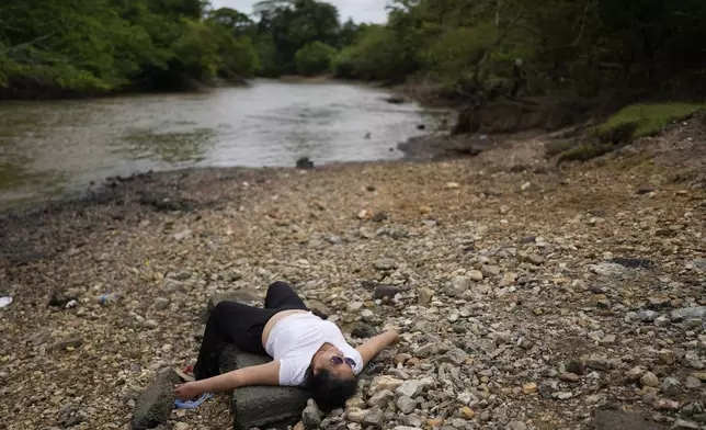 Marisol Jaime, from Venezuela, lies on the shore after disembarking from a boat in Lajas Blancas, Panama, Thursday, Sept. 26, 2024, following her trek through the Darién Gap from Colombia in hopes of reaching the U.S. (AP Photo/Matias Delacroix)