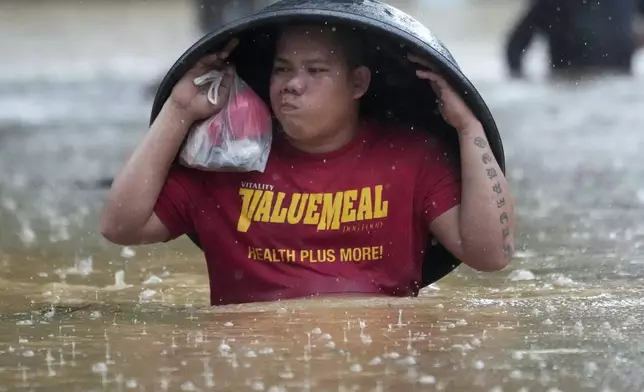 A resident uses a laundry tub to protect him from rain as he wades along a flooded street caused by Tropical Storm Yagi, locally called Enteng, on Monday, Sept. 2, 2024, in Cainta, Rizal province, Philippines. (AP Photo/Aaron Favila)