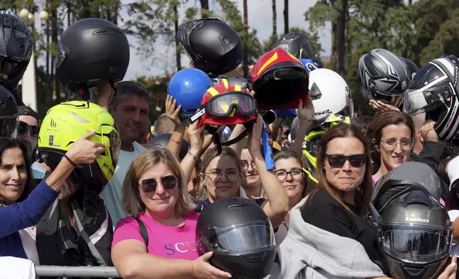 Two red firefighter helmets are held up among motorcyclist helmets being blessed during the IX Pilgrimage of the Blessing of Helmets that draws tens of thousands at the Roman Catholic holy shrine of Fatima, in Fatima, Portugal, Sunday, Sept. 22, 2024. (AP Photo/Ana Brigida)