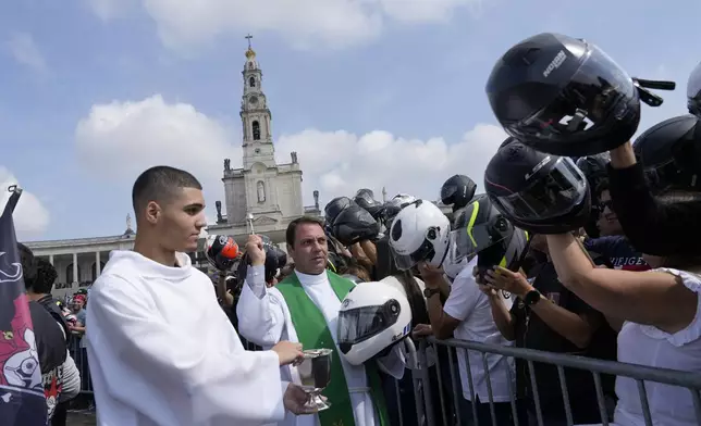 A priest holding a police motorcycling helmet, blesses the helmets of faithful during the IX Pilgrimage of the Blessing of Helmets that draws tens of thousands at the Roman Catholic holy shrine of Fatima, in Fatima, Portugal, Sunday, Sept. 22, 2024. (AP Photo/Ana Brigida)