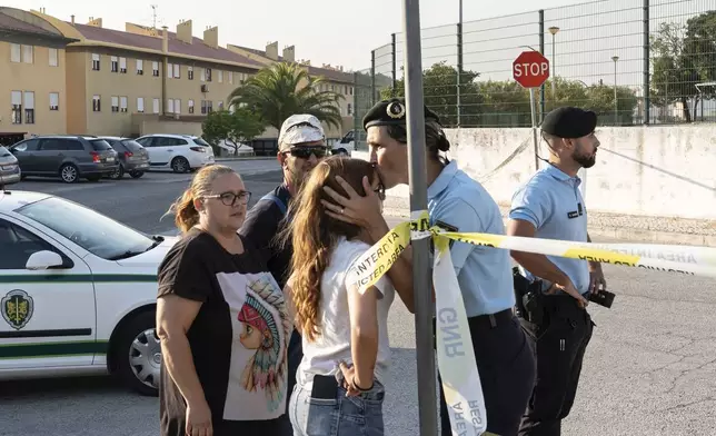 A police officer kisses a girl outside a school where a 12-year-old boy stabbed and injured six other children in Azambuja, near Lisbon, Tuesday, Sept. 17, 2024. (AP Photo/Ana Brigida)