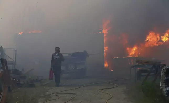 A man carries a fire extinguisher and seeks on the phone while a metalworking warehouse burns in Sever do Vouga, a town in northern Portugal that has been surrounded by forest fires, Monday, Sept. 16, 2024. (AP Photo/Bruno Fonseca)