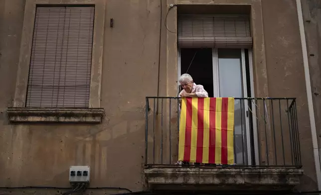 A woman puts a flag of Catalonia on the balcony of her home during the Catalan National Day, during the Catalan National Day, called "Diada", which marks the fall of the Catalan capital to Spanish forces in 1714, in Barcelona, Spain, Wednesday, Sept. 11, 2024. (AP Photo/Emilio Morenatti)