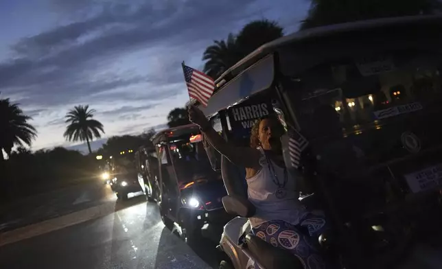 A supporter of Democratic presidential nominee Vice President Kamala Harris waves an American flag and cheers as she participates in a golf cart parade following a campaign event with second gentleman Doug Emhoff, in The Villages, Fla., Friday, Sept. 13, 2024. (AP Photo/Rebecca Blackwell)