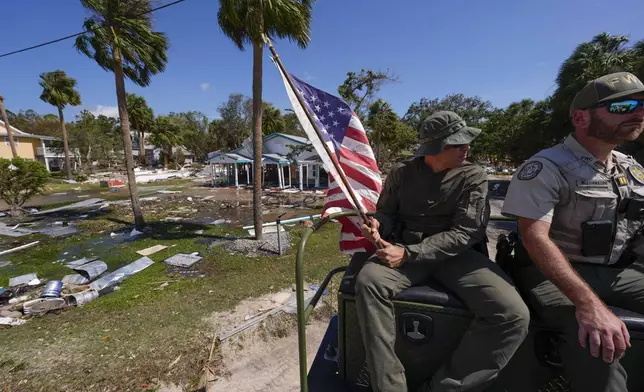 Officer Nate Martir, a law enforcement officer from the Florida Fish Wildlife and Conservation Commission, holds an American flag that was lying on the ground amid debris, while patrolling from a high water capable swamp buggy, in the aftermath of Hurricane Helene, in Cedar Key, Fla., Friday, Sept. 27, 2024. (AP Photo/Gerald Herbert)