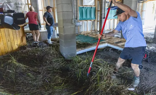 Jansen Pellegrin, right, rakes away marsh grass that floated into a living room area at his family's fishing camp from Hurricane Francine in Terrebonne Parish, La., Thursday, Sept. 12, 2024. (Chris Granger/The Times-Picayune/The New Orleans Advocate via AP)