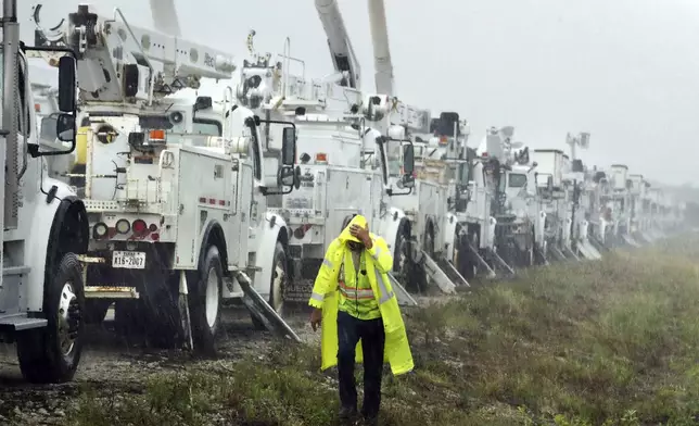 Charles Starling, a lineman with Team Fishel, is pelted with rain as he walks by a row of electrical line trucks stage in a field in The Villages, Fla., Thursday, Sept. 26, 2024, in preparation for damage from Hurricane Helene. (Stephen M. Dowell/Orlando Sentinel via AP)