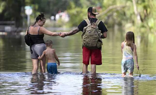 Dustin Holmes, second from right, holds hands with his girlfriend, Hailey Morgan, while returning to their flooded home with her children Aria Skye Hall, 7, right, and Kyle Ross, 4, in the aftermath of Hurricane Helene, Friday, Sept. 27, 2024, in Crystal River, Fla. (AP Photo/Phelan M. Ebenhack)