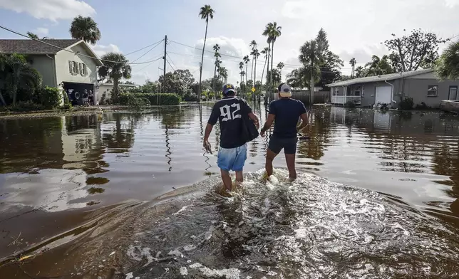 Thomas Chaves, left, and Vinny Almeida walk through floodwaters from Hurricane Helene in an attempt to reach Chaves's mother's house in the Shore Acres neighborhood Friday, Sept. 27, 2024, in St. Petersburg, Fla. (AP Photo/Mike Carlson)