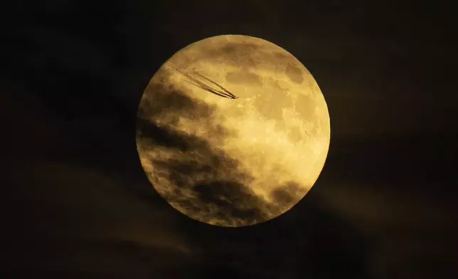 An airplane flies past the moon as it rises in the sky in Istanbul, Turkey, Tuesday, Sept. 17, 2024. (AP Photo/Francisco Seco)