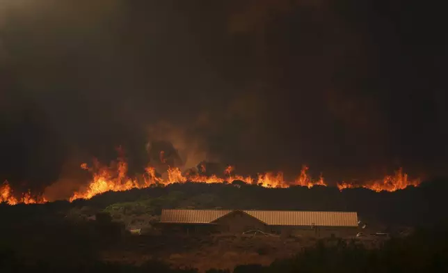 The Airport Fire crests over a structure Tuesday, Sept. 10, 2024, in El Cariso, an unincorporated community in Riverside County, Calif. (AP Photo/Eric Thayer)