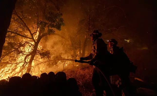 Firefighters establish a defense perimeter around a house threatened by the Bridge Fire in Wrightwood, Calif., Tuesday, Sept. 10, 2024. (AP Photo/Etienne Laurent)