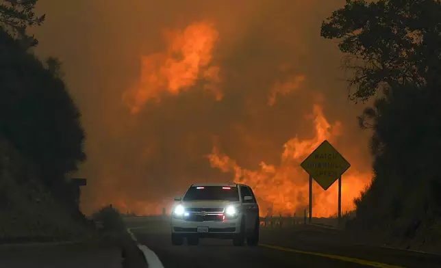 FILE - The Line Fire jumps Highway 330 as an emergency vehicle is driven past Saturday, Sept. 7, 2024, near Running Springs, Calif. (AP Photo/Eric Thayer, File)