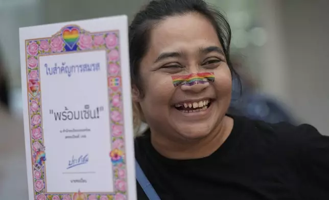 A participant smiles while holding a poster celebrating equality in marriage in Bangkok, Thailand, Wednesday, Sept. 25, 2024. (AP Photo/Sakchai Lalit)