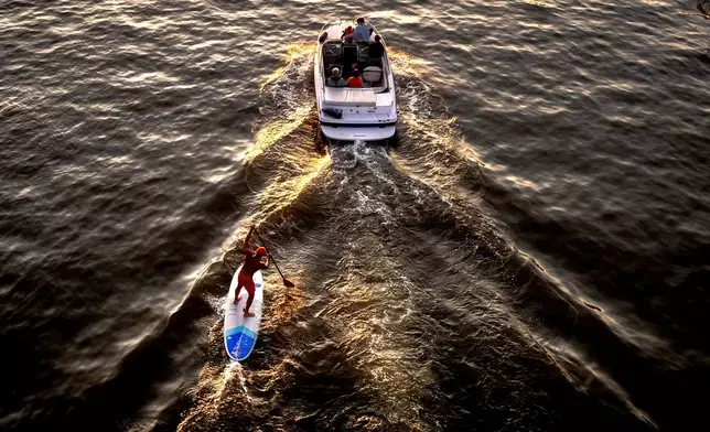 A standup paddler follows the wake of a motor boat on the river Main in Frankfurt, Germany, Friday, Sept. 20, 2024. (AP Photo/Michael Probst)