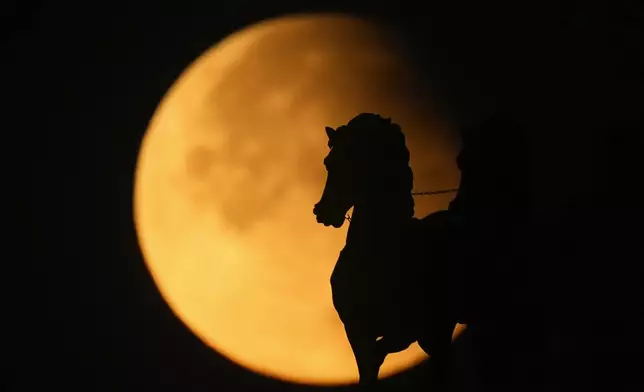 A supermoon rises behind a horse statue atop of Triumphal Arc during a partial lunar eclipse in Moscow, Russia, Wednesday, Sept. 18, 2024. (AP Photo/Pavel Bednyakov)