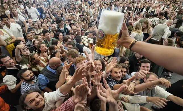 Festival goer reach out for the first glasses of beer on day one of the 189th 'Oktoberfest' beer festival in Munich, Germany, Saturday, Sept. 21, 2024. (AP Photo/Matthias Schrader)