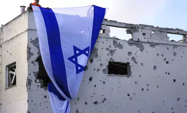 Municipality workers hang an Israeli flag over a damaged building that was hit by a rocket fired from Lebanon, in Kiryat Bialik, northern Israel, on Sunday, Sept. 22, 2024. (AP Photo//Ariel Schalit)