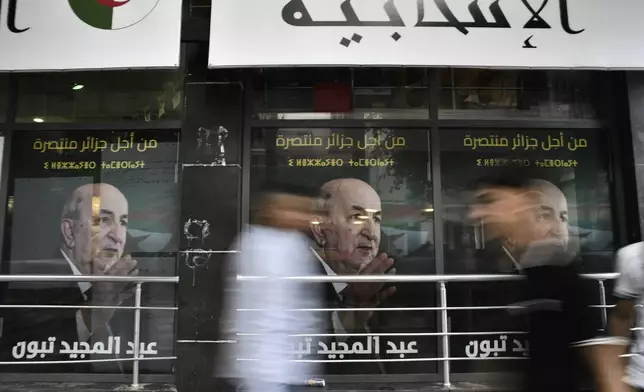 People walk past posters of Algerian President Abdelmadjid Tebboune, after the presidential election results were announced, Sunday, Sept. 8, 2024, in the capital Algiers. (AP Photo/Fateh Guidoum)