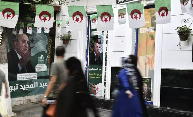 People walk past posters of Algerian President Abdelmadjid Tebboune, after the presidential elections results were announced and Tebboune being declared the winner of Algeria's election, Sunday, Sept. 8, 2024, in the capital Algiers. (AP Photo/Fateh Guidoum)