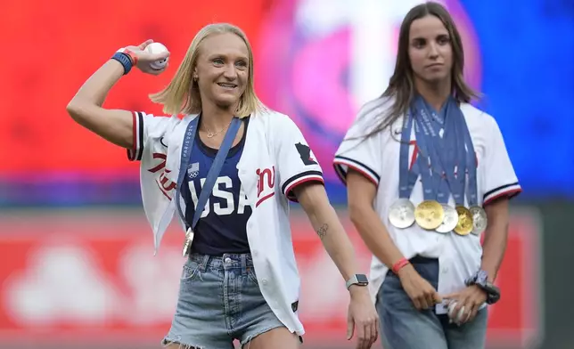 Olympian Sarah Bacon, left, throws the ceremonial first pitch as olympian Regan Smith watches before a baseball game between the Los Angeles Angels and Minnesota Twins, Wednesday, Sept. 11, 2024, in Minneapolis. (AP Photo/Abbie Parr)