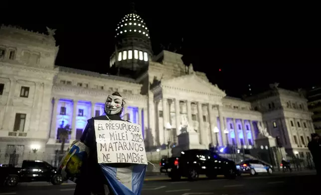 A demonstrator holds a banner that reads in Spanish "The 2025 budget, starving us to death" as Argentina's President Javier Milei presents next year's budget in Congress in Buenos Aires, Argentina, Sunday, Sept. 15, 2024. (AP Photo/Natacha Pisarenko)