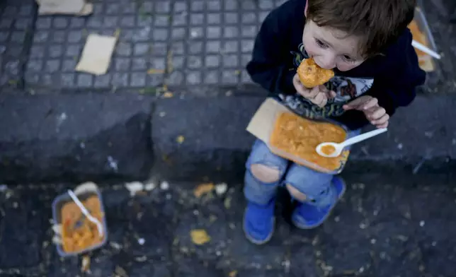 A child eats a free, hot meal on the curb of a soup kitchen on the outskirts of Buenos Aires, Argentina, Thursday, Sept. 12, 2024. (AP Photo/Natacha Pisarenko)