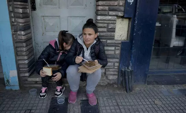 Street vendor Miriam Sidimarco and her daughter Tiziana sit on a door's stoop, to eat a free, cooked meal near the soup kitchen where they received it on the outskirts of Buenos Aires, Argentina, Friday, Sept. 6, 2024. (AP Photo/Natacha Pisarenko)